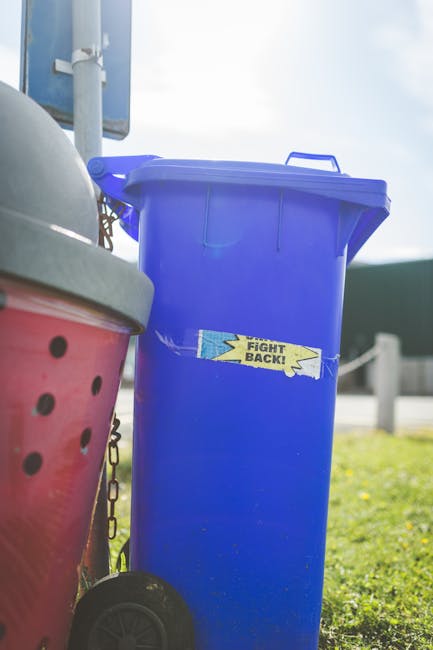 A large collection of overflowing rubbish bins and loose waste scattered across the pavement next to a parked grey car on a paved street. The waste includes black, black with white logo, and red plast